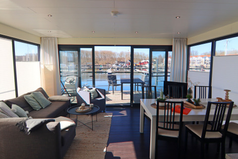 Stue og spiseområde på husbåd Family & Friends LP 3 med udsigt over vandet og havnen i Tyskland.