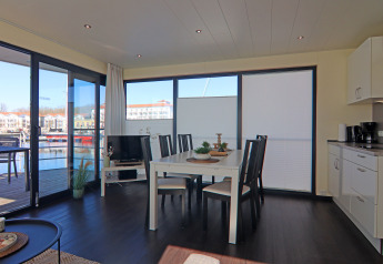 Bright, modern living and dining area on a houseboat with large windows overlooking the marina in Germany.