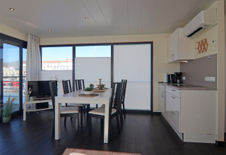 Zona pranzo e soggiorno moderna su una houseboat con grandi finestre, cucina e arredo luminoso in Germania.