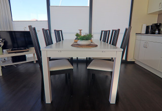 Sala da pranzo su una houseboat con tavolo bianco, sedie nere e grandi finestre accanto alla cucina moderna.
