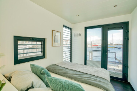 Camera da letto su una casa galleggiante con letto matrimoniale, ampie finestre e vista sul porto in Germania.
