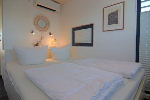 Camera moderna di una houseboat con letto matrimoniale, cuscini bianchi, arte murale e finestra.
