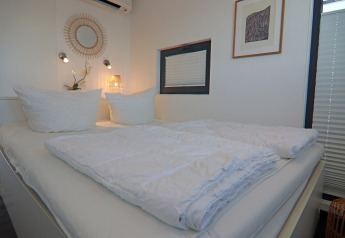 Slaapkamer op een woonboot met fris wit beddengoed, trendy decoratie en warme, sfeervolle verlichting.