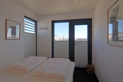 Camera da letto su una casa galleggiante con letto matrimoniale, grandi finestre, arte moderna e vista sul porto.