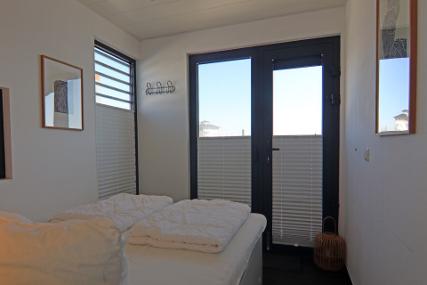 Chambre sur une péniche avec lit double, grandes fenêtres, literie blanche et décorations murales modernes.