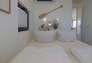 Dormitorio en una casa flotante con cama doble, dos almohadas, decoración de pared y ventana.