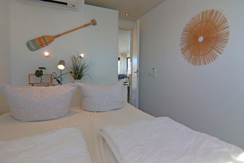 Bedroom on a houseboat with white bedding, potted plants, wall decor, and a cozy, nautical vibe.