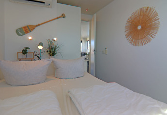 Slaapkamer op een woonboot met wit beddengoed, planten en een decoratief wandornament.