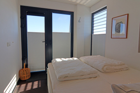 Bedroom on a houseboat with a double bed, French doors, modern minimalist decor, and natural daylight.