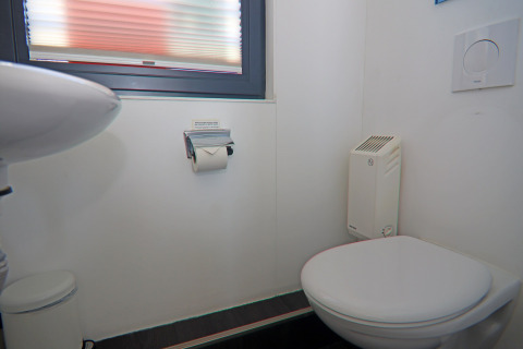 Moderne, compacte badkamer op een woonboot met zwevend toilet, kleine lavabo, kachel en raam erboven.