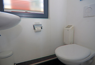 Bagno compatto e moderno su una houseboat con WC sospeso, piccolo lavandino, stufetta e finestra sopra.