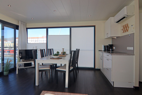 Soggiorno e cucina moderni su una houseboat con zona pranzo, ampie finestre e vista sull'acqua.