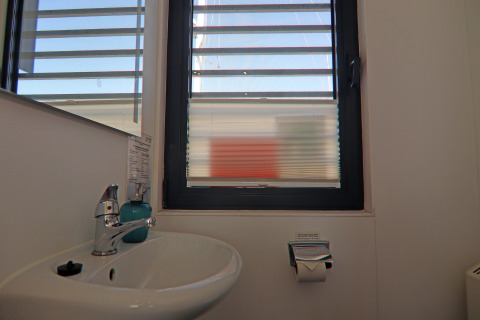 Wastafel met spiegel, raam met jaloezieën en toiletrolhouder op een woonboot in Duitsland.