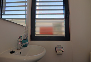 Sink with mirror, window with blinds, and toilet paper holder on a houseboat in Germany.