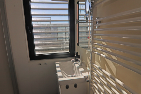 Piccolo bagno su una houseboat con finestra, lavandino compatto e specchio a parete illuminati dal sole.