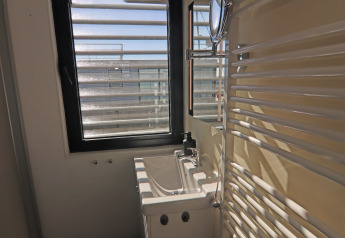 Kleine badkamer op een woonboot met raam, compacte wastafel en wandspiegel, zonlicht straalt binnen.