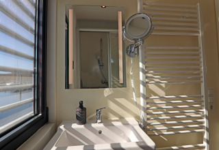 Bagno di una houseboat con lavandino, specchio, dispenser di sapone e vista sull'acqua dalla finestra.