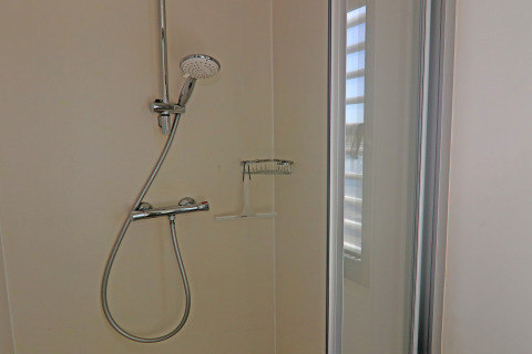 Modern shower inside a houseboat bathroom, featuring a glass door, window, and chrome shower fixtures.