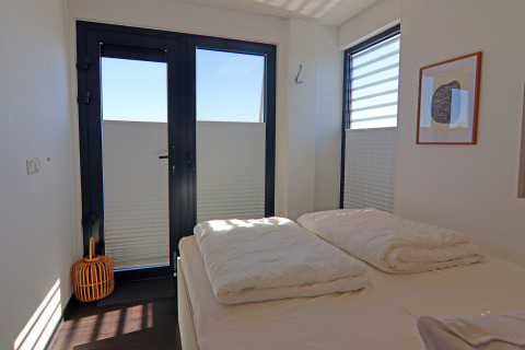Camera da letto moderna su una houseboat con porte a vetro, grandi finestre ed arredo minimalista.