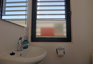Bathroom on a houseboat with a sink, soap dispenser, toilet paper roll, and window showing the view outside.