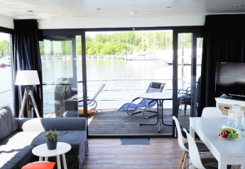 Intérieur d'une péniche moderne avec salon, salle à manger et vue sur la terrasse et l'eau par baie vitrée.