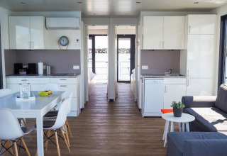 Modern houseboat interior with kitchen, dining table, living area, and access to a deck overlooking water.