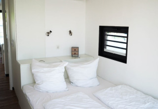 Sleeping area on a houseboat with white pillows, modern reading lamps, and a small window on the wall.