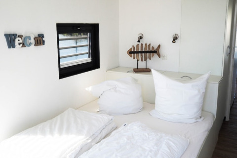 Bright bedroom on a houseboat with white pillows, a fish decor piece, wall lamps, and a window view.