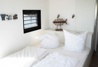 Dormitorio luminoso en una casa flotante con almohadas blancas, decoración de pez y ventana al agua.