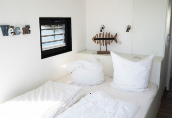 Bright bedroom on a houseboat with white pillows, a fish decor piece, wall lamps, and a window view.