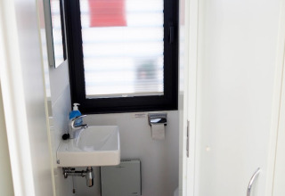Pequeño baño en una casa flotante con lavabo blanco, dosificador de jabón azul, ventana y portarrollo.
