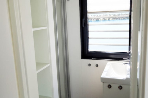 Baño luminoso y compacto en una casa flotante con estantería blanca, lavabo pequeño y ventana con vista al agua.