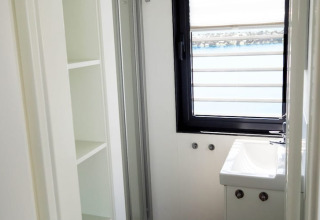 Bagno luminoso e compatto su una houseboat con scaffali bianchi, piccolo lavandino e finestra vista acqua.