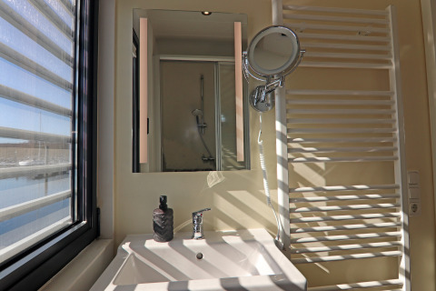 Bright houseboat bathroom with window, sink, mirror, towel warmer, and view of a marina in daylight.