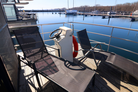 Pont ensoleillé du houseboat 'Family & Friends LP' avec chaises longues, barre et vue sur la marina en Allemagne.