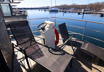 Pont ensoleillé du houseboat 'Family & Friends LP' avec chaises longues, barre et vue sur la marina en Allemagne.