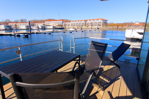 View from a houseboat deck featuring table, chairs, and a marina in the background on a sunny day.
