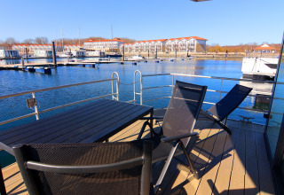 View from a houseboat deck featuring table, chairs, and a marina in the background on a sunny day.