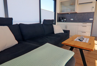 Cozy houseboat living area with a dark sofa, light pillows, a wooden table, and a modern kitchenette.