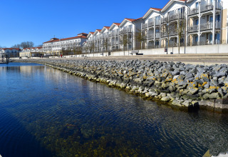 Vista da una houseboat al molo, con edifici bianchi sullo sfondo e acqua blu limpida in Germania.
