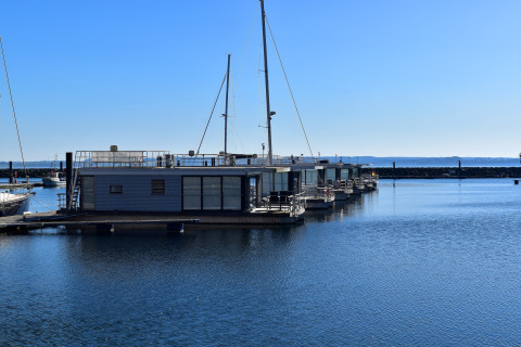 Foto de casas flotantes atracadas en un puerto tranquilo, cielo azul y agua clara en un día soleado.
