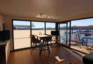 Modern houseboat interior with large windows, dining area, and sunny views of the harbor and water.