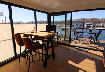 Innenaufnahme eines Hausboots mit Esstisch und Stühlen, Blick auf das Deck und den Jachthafen.