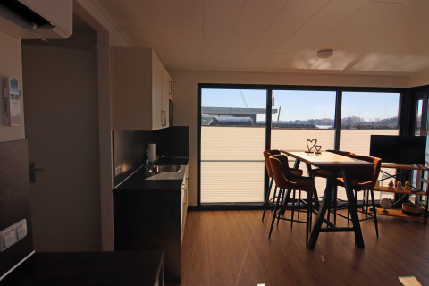 Modern houseboat interior featuring a kitchen, dining table, and large windows overlooking the water view.