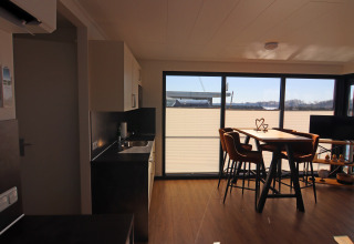 Modern houseboat interior featuring a kitchen, dining table, and large windows overlooking the water view.