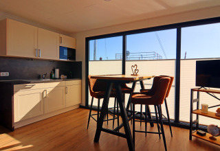 Modern kitchen and dining area inside a houseboat with large windows letting in bright natural light.