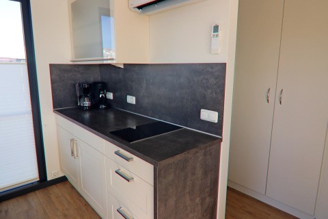 Modern kitchenette on a houseboat featuring a stovetop, coffee maker, white cabinets, and dark countertop.