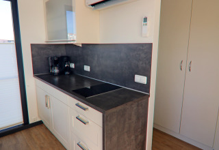 Modern kitchenette on a houseboat featuring a stovetop, coffee maker, white cabinets, and dark countertop.