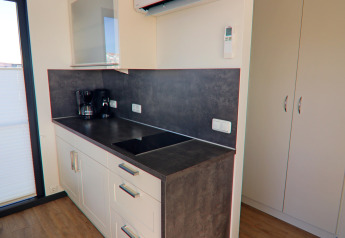 Modern kitchenette on a houseboat featuring a stovetop, coffee maker, white cabinets, and dark countertop.