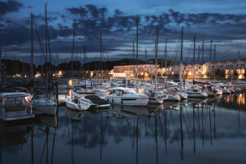 Evening photo of yachts and houseboats docked at Houseboat Family & Friends with lights in Germany.